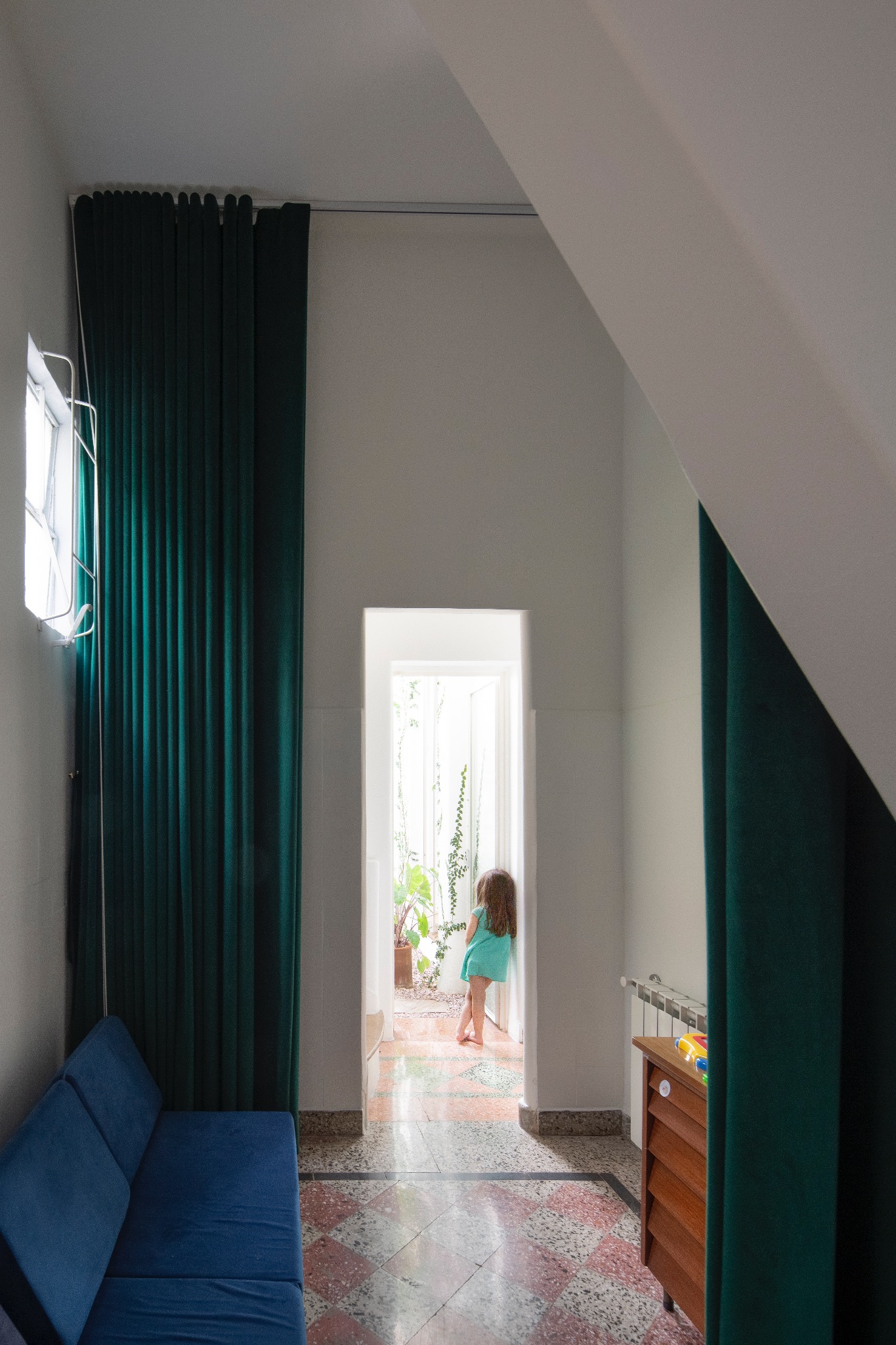Interior de doble altura con cortinas verdes y visual hacia el patio
